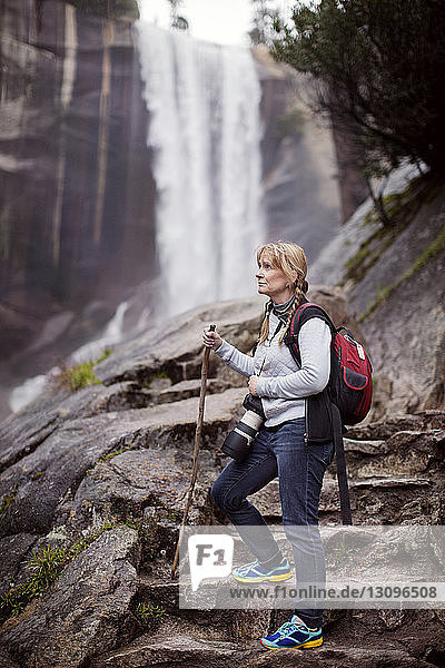Nachdenkliche Frau wandert im Wald gegen Wasserfall
