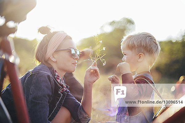 Side view of mother giving flowers to son on field during sunny day