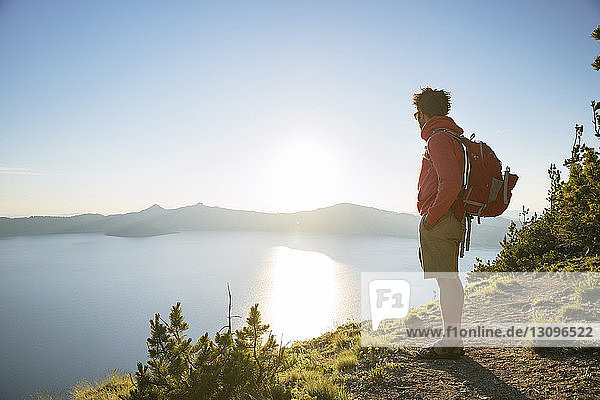 Hiker with backpack standing on mountain at Crater Lake National Park during sunny day