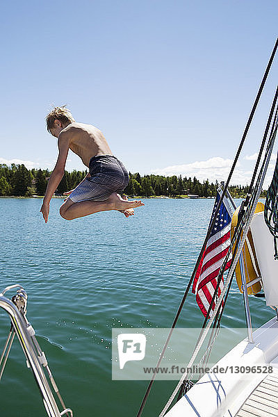 Boy jumping from sailboat in sea against blue sky