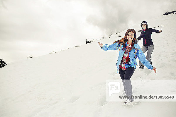 Fröhliche Freundinnen rennen auf schneebedecktem Berg gegen die Wolken