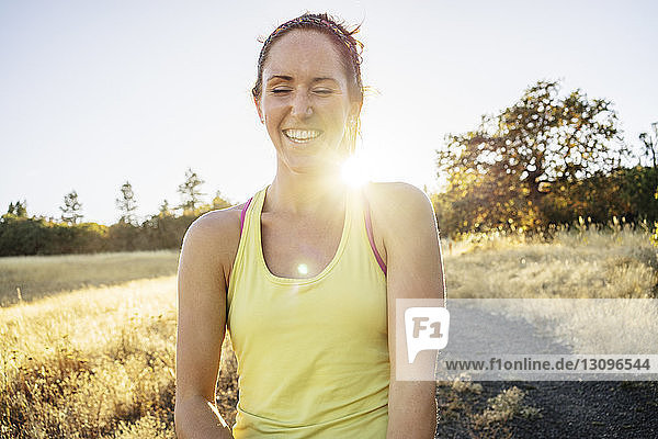 Frau lächelt  während sie am sonnigen Tag auf dem Feld gegen den klaren Himmel steht