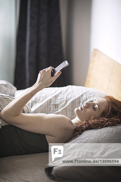 Hochwinkelansicht einer Frau  die telefoniert  während sie auf dem Bett liegt