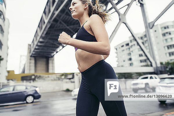 Low angle view of determined female athlete running on street under Oakland Bay Bridge