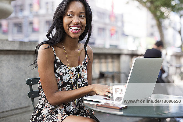 Cheerful woman using laptop at sidewalk cafe