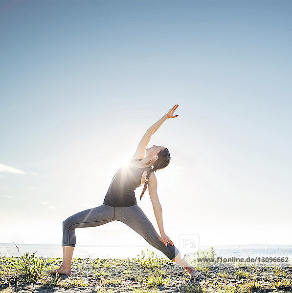 Frau praktiziert Yoga mit erweitertem Seitenwinkel am Strand bei sonnigem Wetter