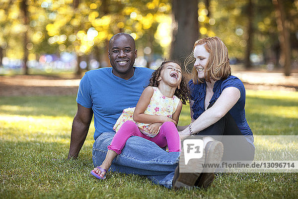 Glückliche Frau kitzelt Tochter  die auf dem Schoss eines Mannes sitzt