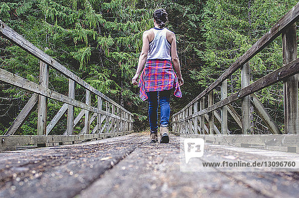 Rear view of woman walking on footbridge amidst trees in forest