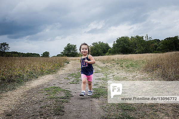 Kleines Mädchen rennt auf Feld gegen bewölkten Himmel