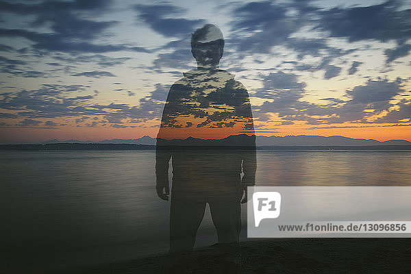 Double exposure of man standing at beach against cloudy sky during sunset