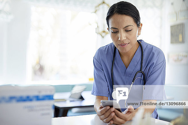 Ärztin mit Stethoskop  die während der Arbeit im Krankenhaus ein Smartphone benutzt