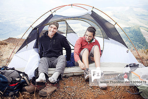 Happy couple sitting in tent on mountain