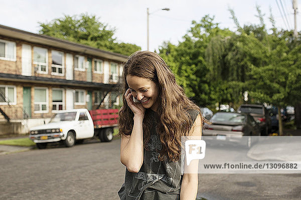 Lächelnde Frau spricht am Mobiltelefon  während sie an Gebäuden steht