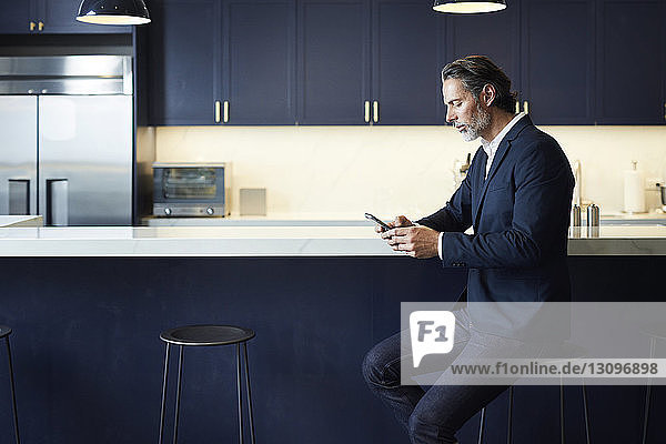 Geschäftsmann benutzt ein Smartphone  während er auf einem Hocker an der Küchentheke im Kreativbüro sitzt