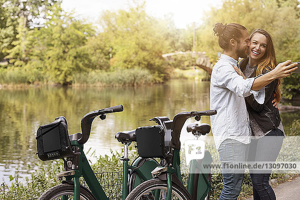 Man taking selfie while kissing girlfriend by lake