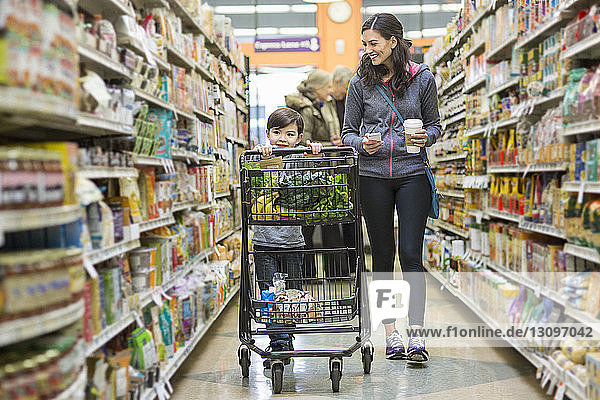 Frau geht mit ihrem Sohn mit Einkaufswagen im Supermarkt