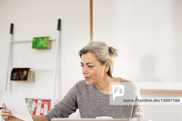 Concentrated woman holding paper while working at home