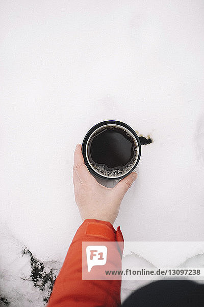 Abgehackte Hand einer Frau  die schwarzen Kaffee in einer Tasse auf Schnee hält