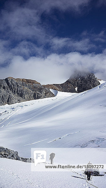 Männer wandern auf schneebedecktem Berg gegen den Himmel