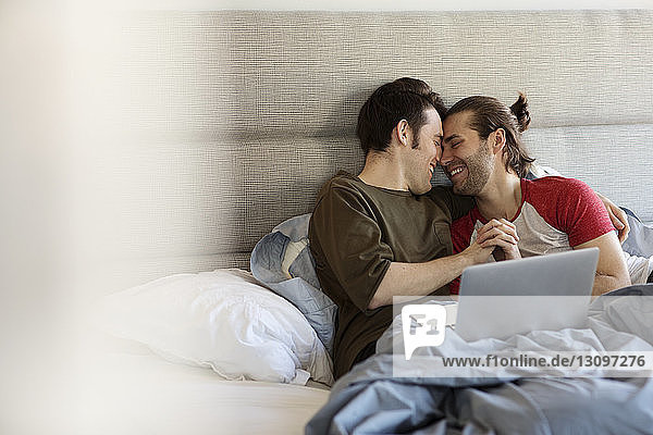 Happy homosexual couple romancing on bed at home