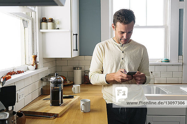 Man using smart phone while leaning by kitchen counter at home