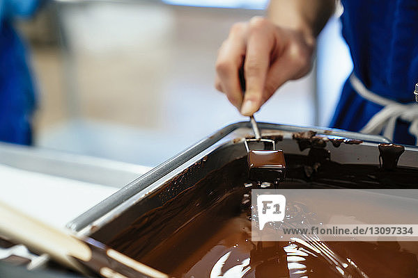 Geschorene Hand einer Köchin  die in der Fabrik Schokolade in Fondue taucht