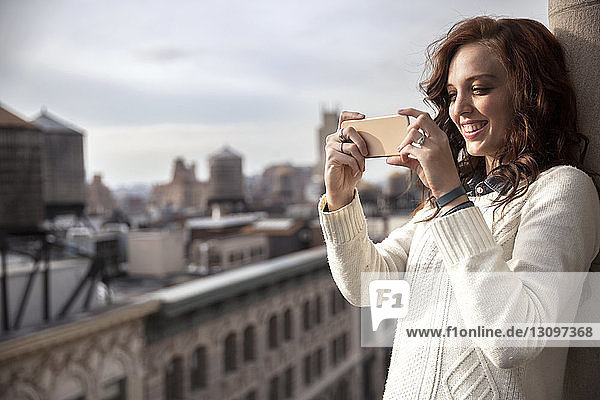 Lächelnde Frau fotografiert mit Smartphone auf dem Balkon