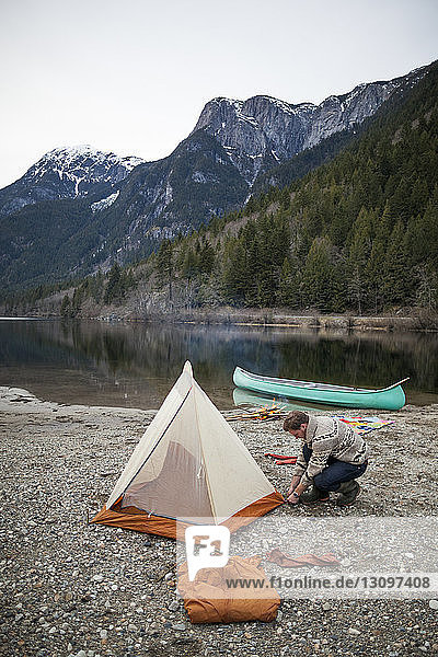 Hochwinkelansicht eines Mannes  der am Seeufer ein Zelt gegen Berge baut