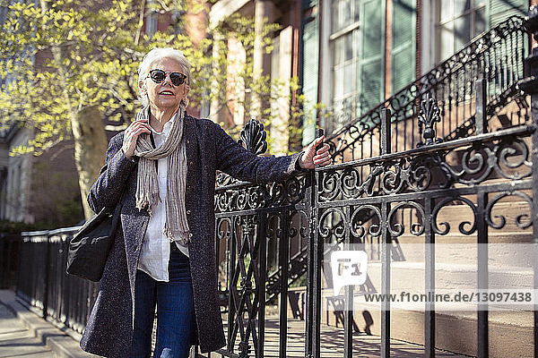 Nachdenkliche ältere Frau steht am Metallgeländer auf der Straße