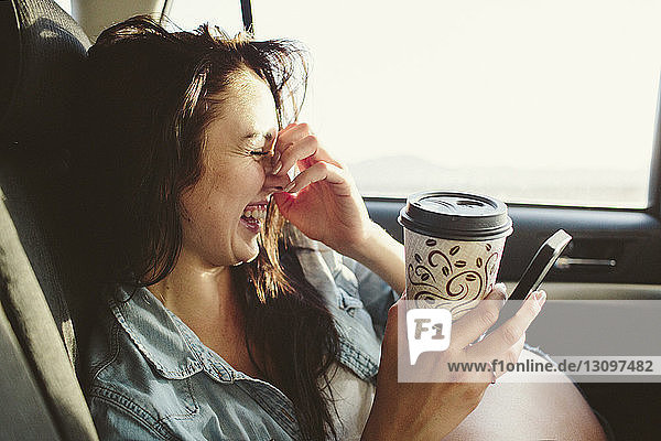 Glückliche Frau mit Kaffeetasse  die während einer Autofahrt mit dem Handy telefoniert