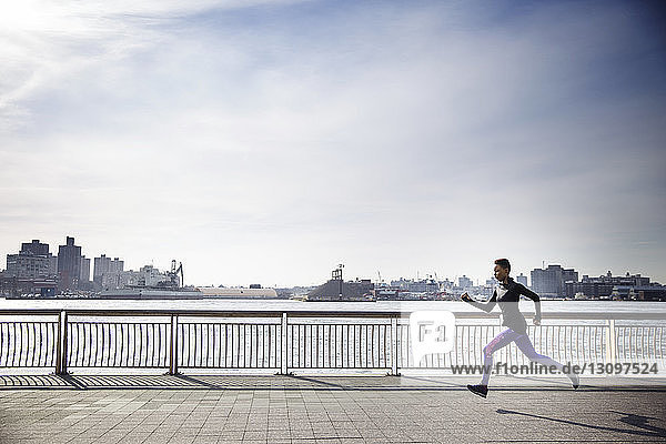 Seitenansicht einer entschlossenen Sportlerin  die auf einem Fußweg am Fluss gegen den Himmel läuft