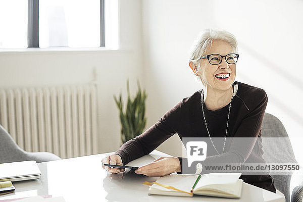 Lächelnde ältere Geschäftsfrau hält Tablette und schaut im Amt weg