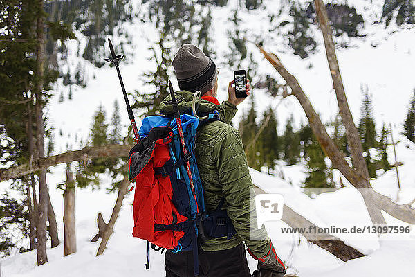 Male hiker photographing while standing on field during winter