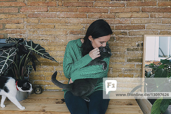 Frau küsst Katze  während sie zu Hause an einer Ziegelmauer sitzt