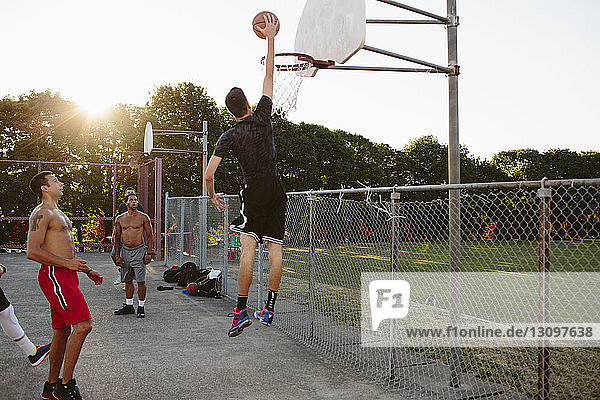 Freunde sehen Mann beim Dunking beim Basketballspielen auf dem Platz