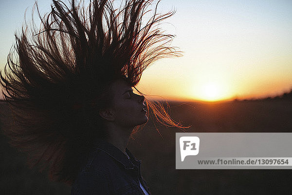 Seitenansicht einer Frau mit geschlossenen Augen  die bei Sonnenuntergang mit den Haaren wirft  während sie am Himmel steht