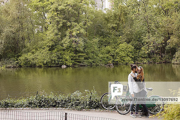 Happy man kissing girlfriend while standing with bicycles by lake