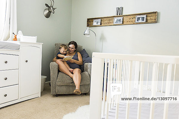 Mutter mit Sohn liest Buch  während sie zu Hause auf einem Stuhl sitzt