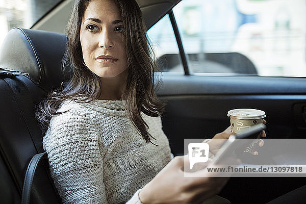 Junge Frau hält Einwegglas und Smartphone im Taxi