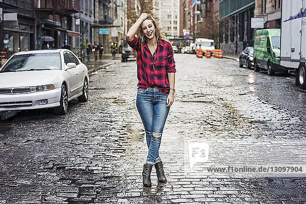 Porträt einer lächelnden Frau  die auf einer nassen Straße inmitten von Gebäuden steht