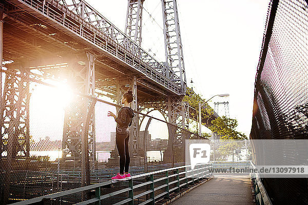 Frau steht auf einem Geländer und schaut an einem sonnigen Tag auf die Williamsburg Bridge