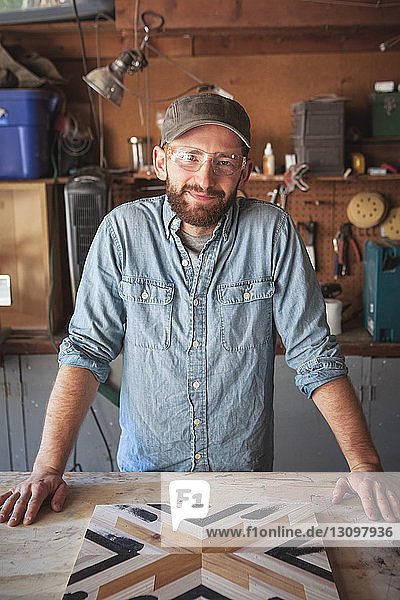 Portrait of smiling craftsperson with wooden art at workbench