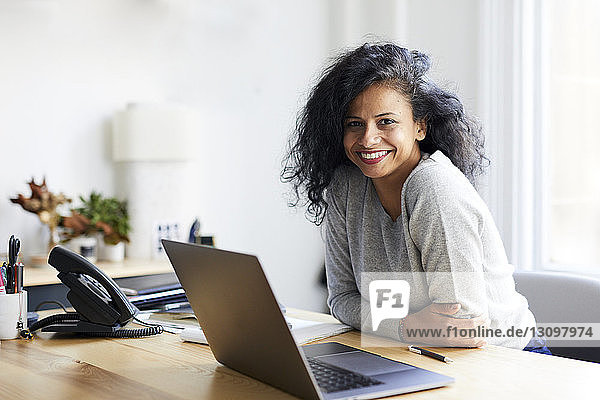 Porträt einer lächelnden Geschäftsfrau mit Laptop-Computer am Schreibtisch im Büro