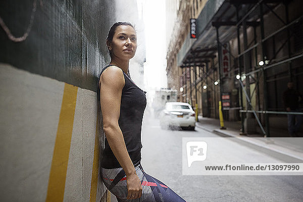 Seitenansicht einer nachdenklichen  sportlichen Frau  die an einer Wand an der Straße lehnt