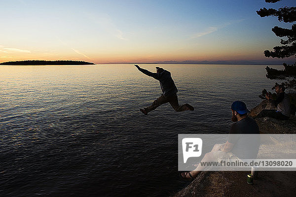 Man jumping at Sucia Island against Strait of Georgia during sunset