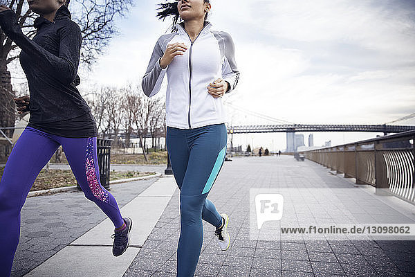 Niedriger Abschnitt von Athletinnen  die auf einem Fußweg mit der Williamsburg-Brücke im Hintergrund laufen