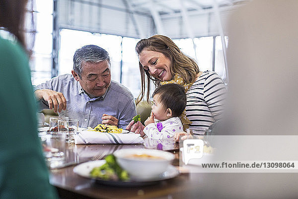 Family looking at cute baby boy eating food in restaurant