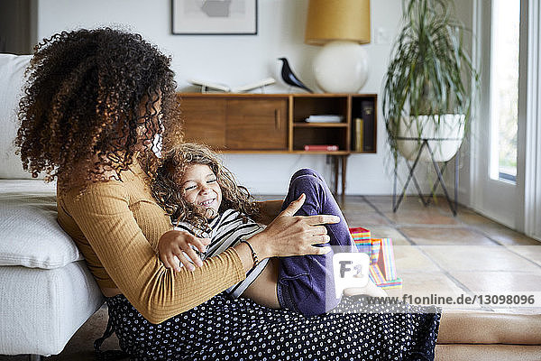 Fröhliche Mutter spielt mit ihrer Tochter  während sie zu Hause auf dem Boden am Sofa sitzt