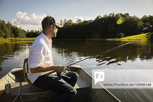 Man fishing while sitting in rowboat on lake