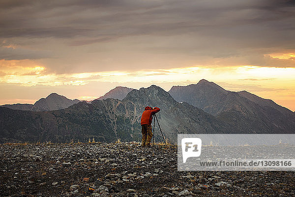 Rear view of man photographing mountains against cloudy sky